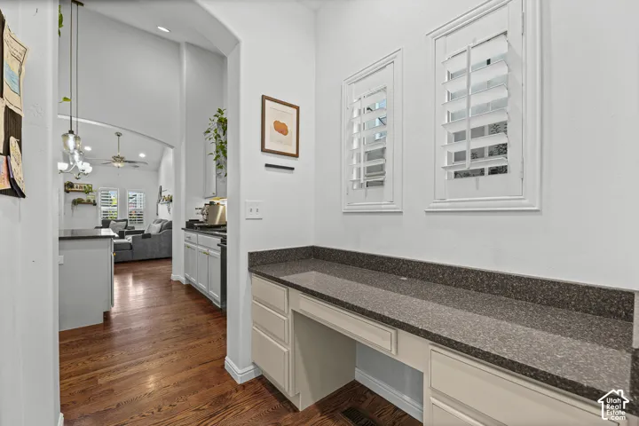 Built-in desk with a speckled countertop, white cabinetry, and two windows with white plantation shutters