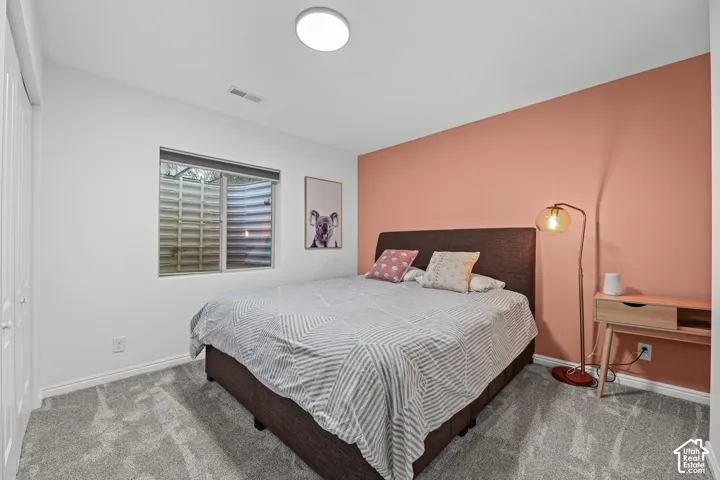 Carpeted flooring, a window with exterior grate, a flush-mount ceiling light fixture, and white bi-fold closet doors