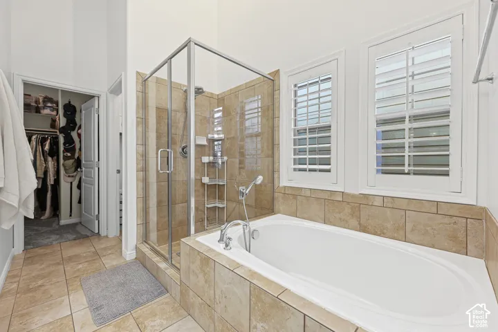 Tile flooring, walk-in shower with glass enclosure, built-in soaking tub, and shuttered windows