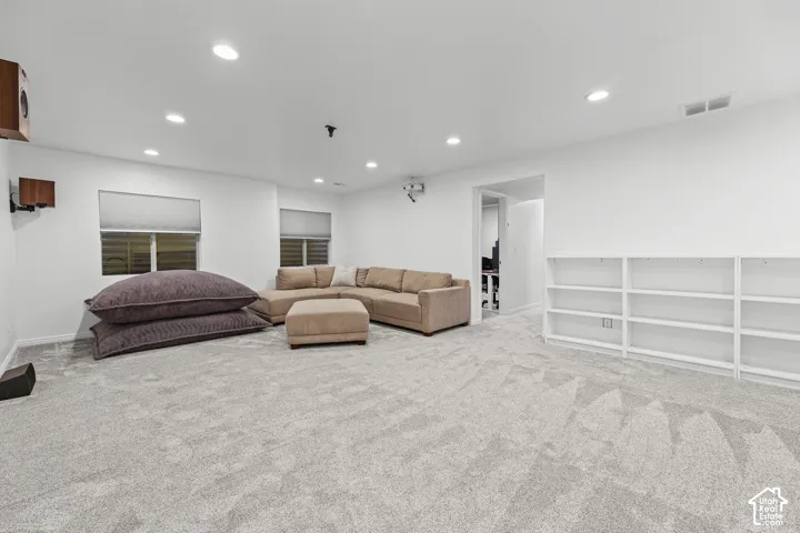 Recessed lighting, wall-mounted speakers, two windows with blinds, a built-in shelving unit, and gray carpeting