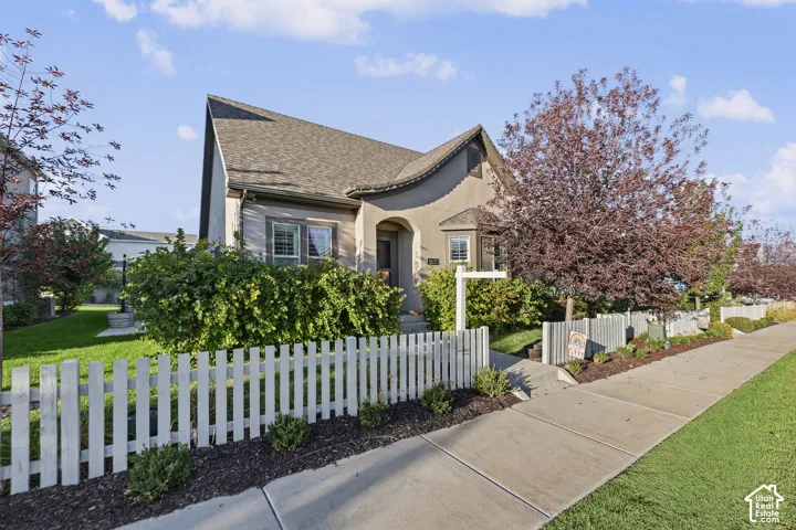 Neutral-toned exterior with distinct roofline, white picket fence, mature trees, and landscaped front yard