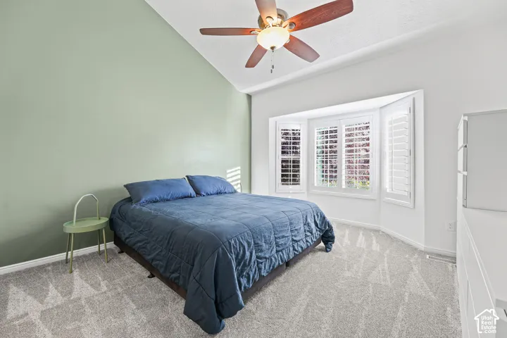 Vaulted ceiling with a ceiling fan, bay window with plantation shutters, and light-toned carpeting