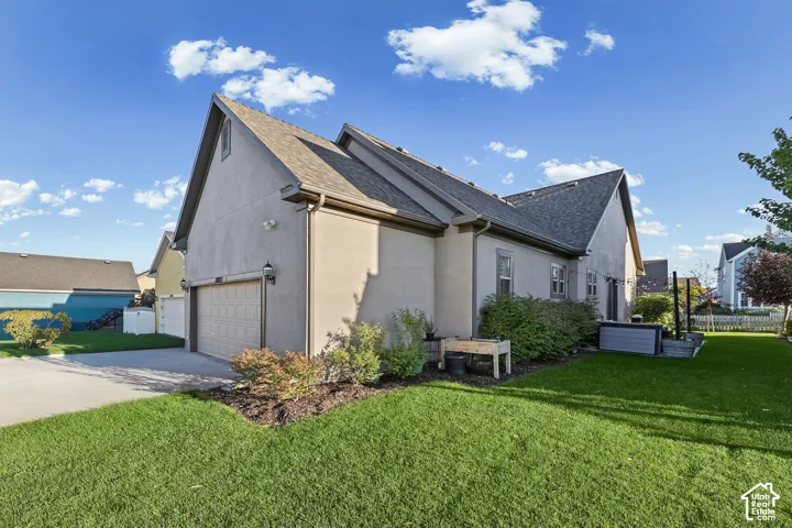 Exterior featuring a tan stucco finish, gabled roofline, attached garage, concrete driveway, and a manicured lawn