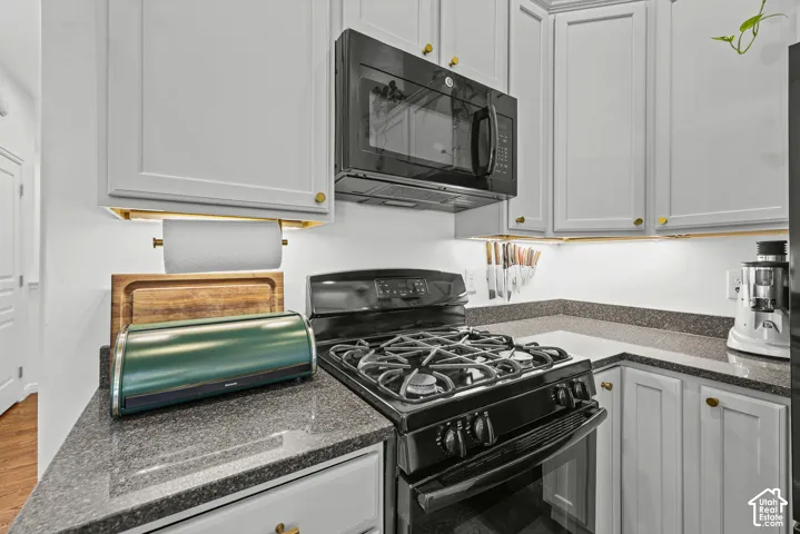 Light gray cabinetry with gold-tone hardware, dark speckled countertops, black gas range, and a built-in black microwave