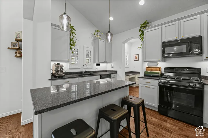 Kitchen featuring a vaulted ceiling, wood-finish flooring, light gray cabinetry, black countertops, and a black gas range with an overhead microwave