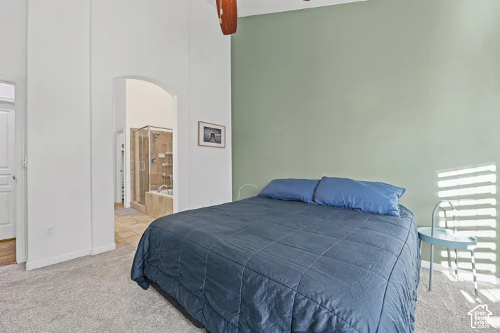 Carpeted room with high ceilings, an arched doorway, and an attached bathroom featuring a glass-enclosed shower and built-in tub