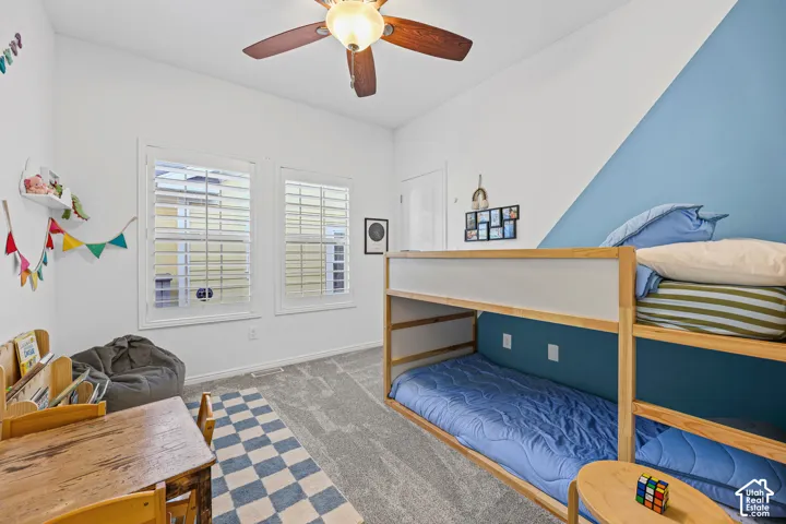 Ceiling fan with a light fixture, dual windows with plantation shutters, carpeted flooring, and a two-tone painted accent wall