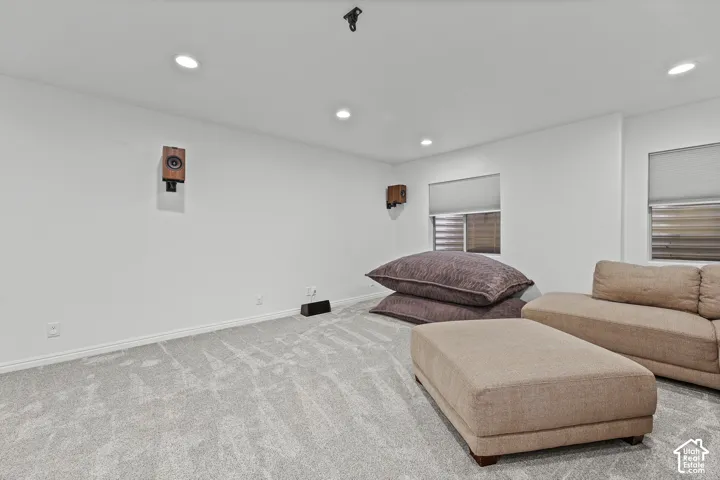 Recessed ceiling lighting, wall-mounted speakers, two windows with blinds, and light-toned carpeting