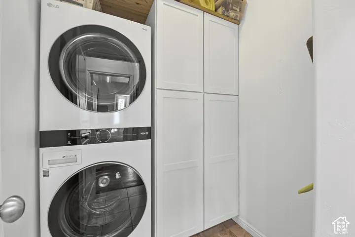 Stackable washer and dryer, white paneled cabinetry, and wood-finish flooring