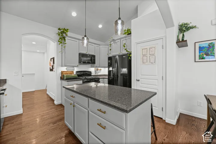 Kitchen featuring light gray cabinetry with brass hardware, black appliances, a central island with a dark countertop, and wood-finish flooring