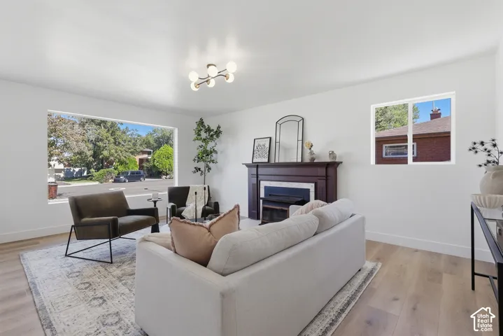 Spacious living area featuring light wood-finish flooring, a contemporary ceiling light fixture, large picture window, and a fireplace with a dark wood mantel