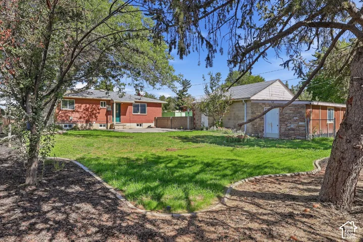 Expansive grassy area with mature trees, a red brick residence, and a stone-clad outbuilding