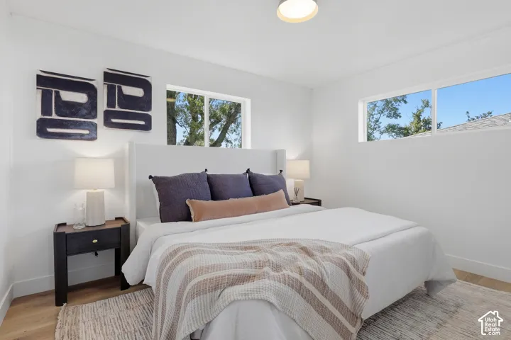 Bright bedroom featuring wood-finish flooring, white walls, and a contemporary ceiling light fixture