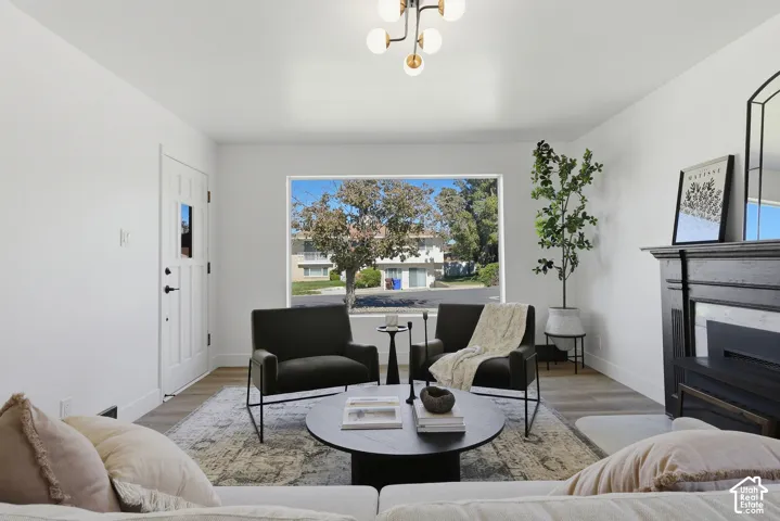 White paneled entry door, contemporary chandelier, large picture window, wood-finish flooring, and a decorative fireplace mantel