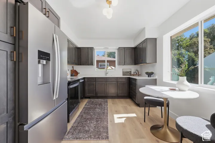 Stainless steel French door refrigerator, dark wood-finish cabinetry, light wood-finish flooring, white countertops, and a built-in electric range