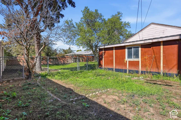 Backyard space featuring a chain-link fence, mature trees, and a building with a window