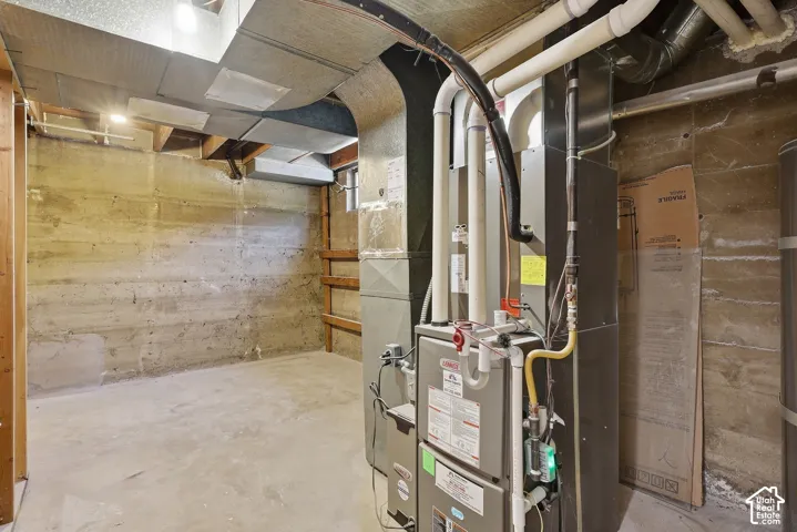 Unfinished basement with concrete flooring and exposed concrete walls, featuring a modern HVAC system, exposed ductwork, and overhead lighting