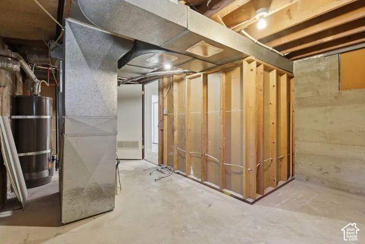 Concrete flooring with exposed ceiling joists and unfinished framing, featuring a water heater and visible ductwork