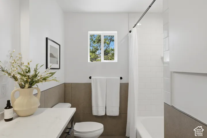 Bathroom featuring a white subway tile shower, a fixed window, a vanity with a light-colored countertop, and a built-in toilet