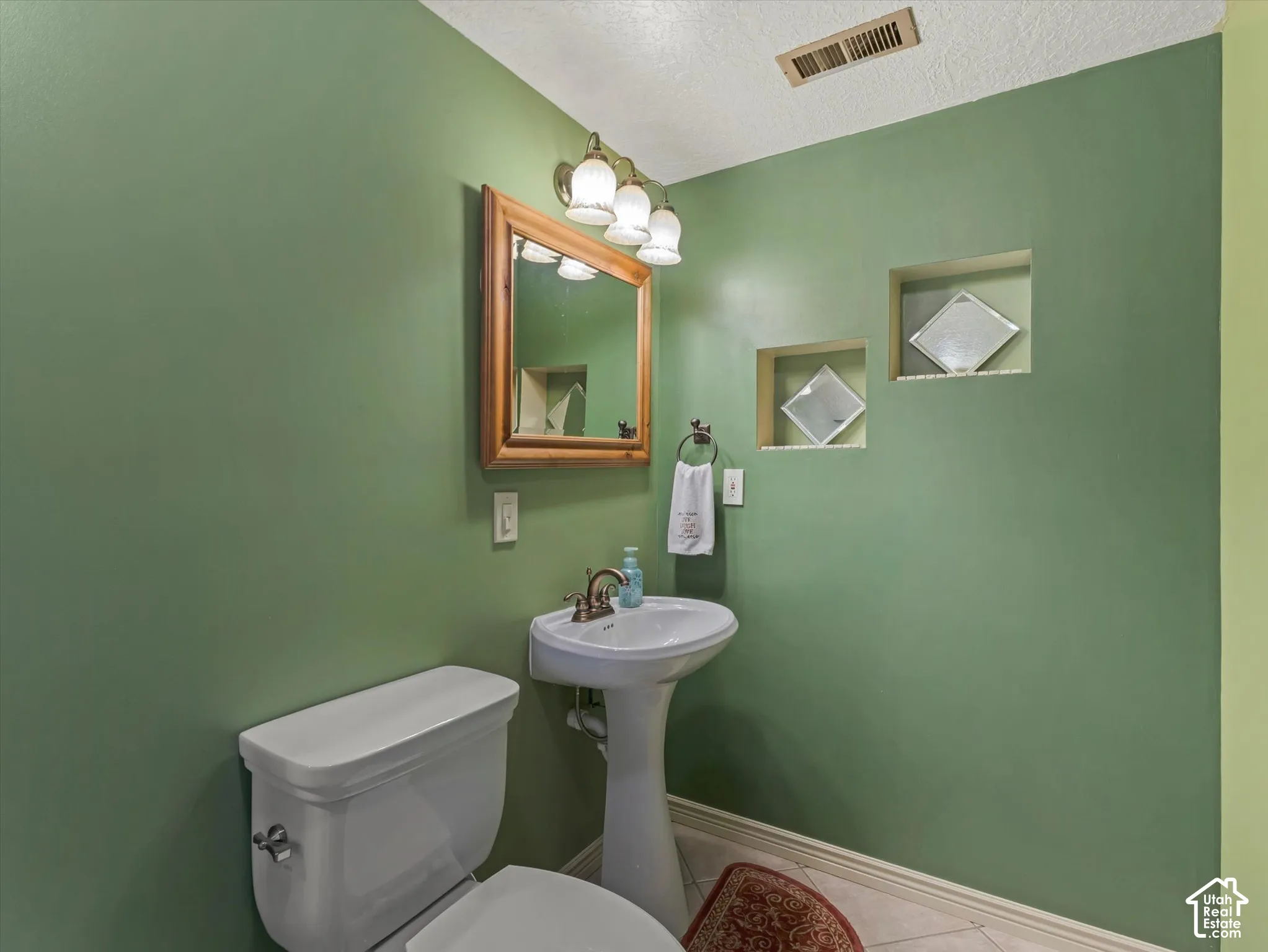 Pedestal sink with a white basin, wood-framed mirror, and recessed wall shelving