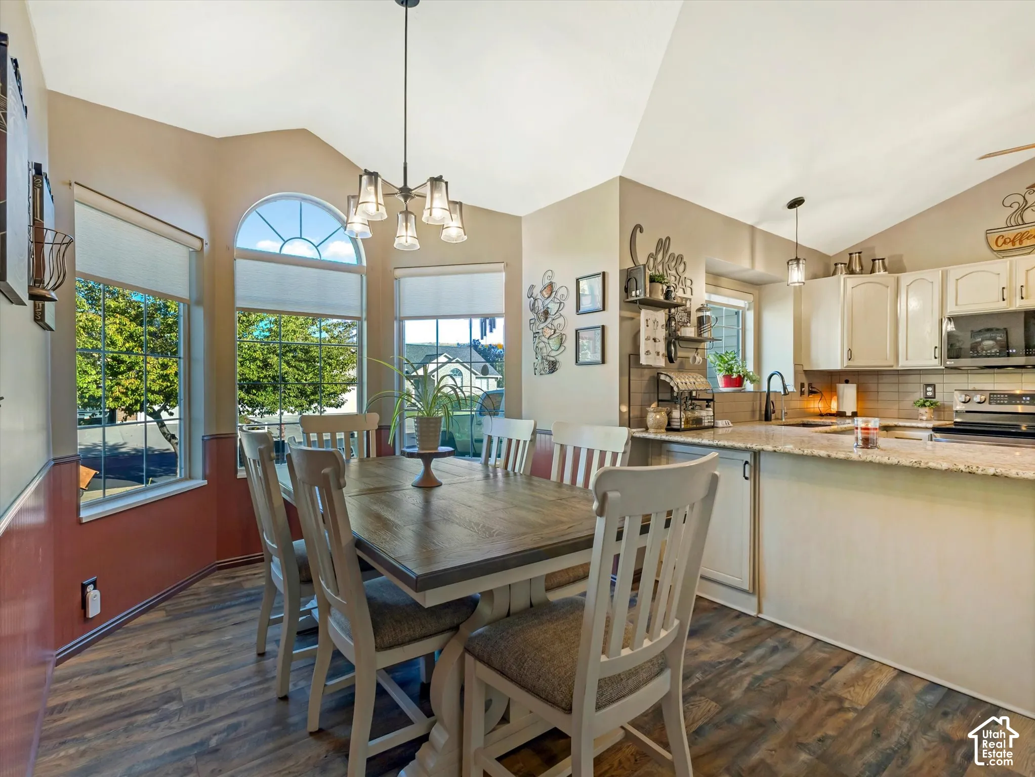 Vaulted ceiling with an architectural window, wood-finish flooring, and a kitchen featuring light-toned cabinetry and stone-finish countertops