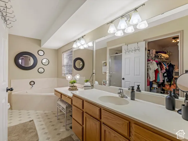 Dual basin vanity with light wood cabinetry, a large soaking tub, and a shower with a sliding glass door