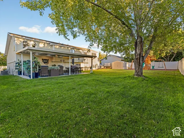 Expansive backyard featuring a manicured lawn, a mature tree, and a covered patio area with a concrete slab