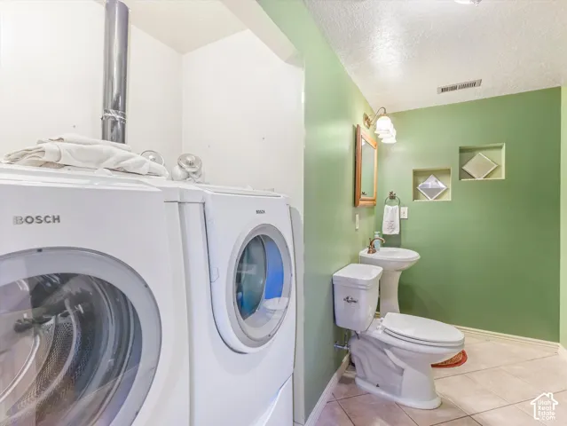 Pedestal sink with wall-mounted mirror, recessed wall niches, and tile flooring