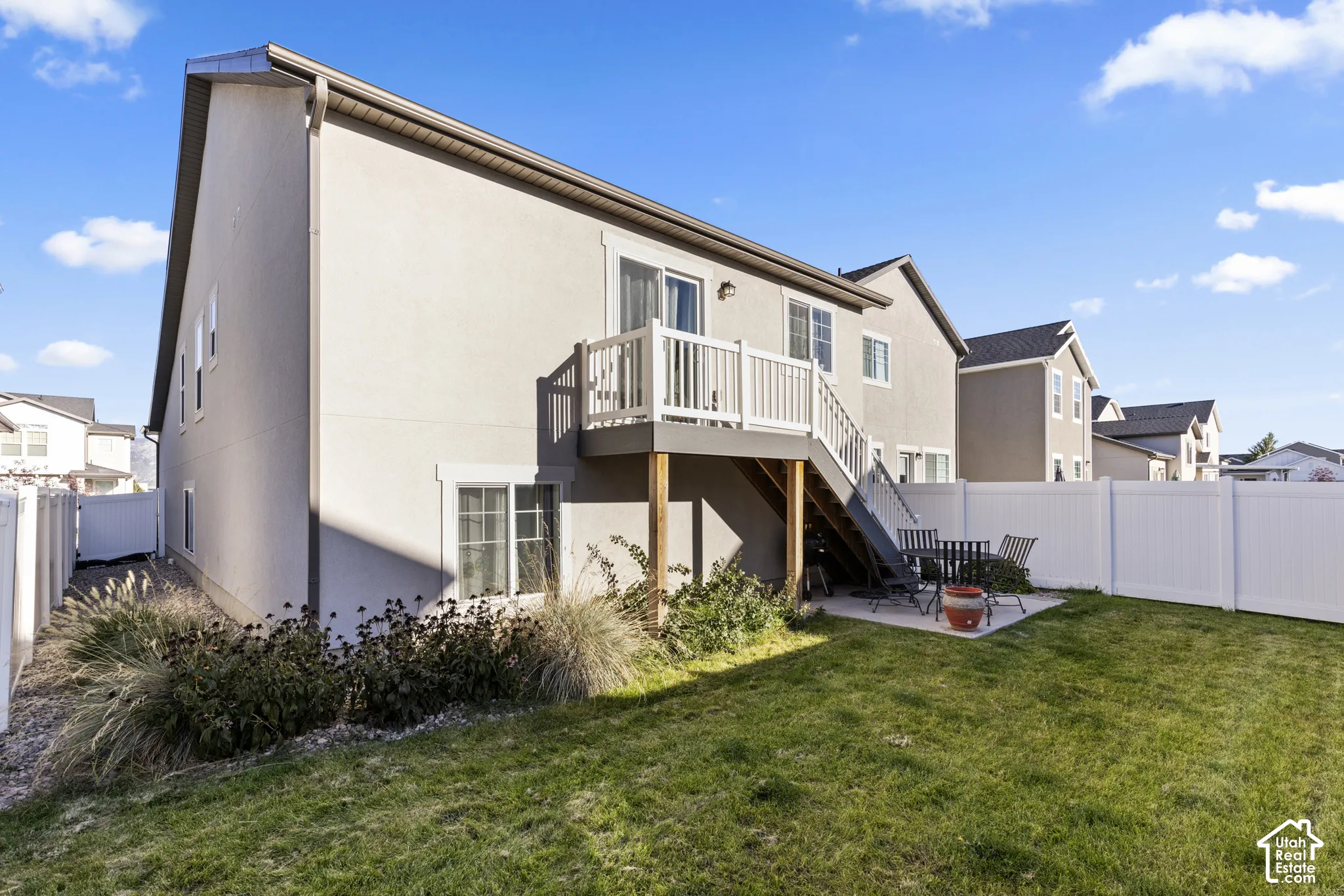 Exterior featuring a stucco finish, second-story balcony with white railings, ground-level concrete patio, fenced yard with a white privacy fence, and manicured lawn