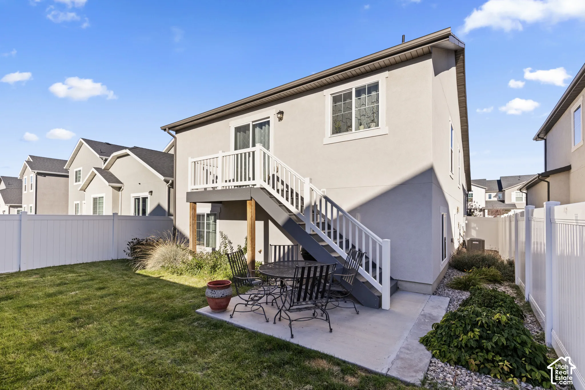 Stucco exterior with a second-story deck, ground-level patio, and a manicured lawn