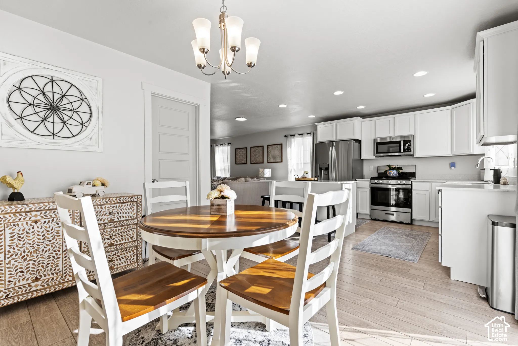 Recessed lighting, wood-finish flooring, white cabinetry, stainless steel appliances, and a central chandelier