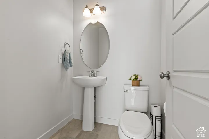 White pedestal sink with a chrome faucet, oval wall mirror, and overhead vanity lighting