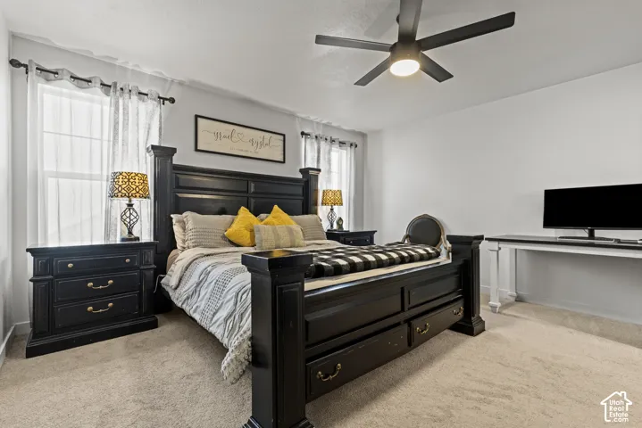 Ceiling fan with integrated lighting, window with sheer curtains, neutral wall paint, and carpeted flooring