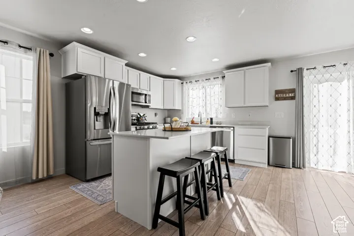 Kitchen featuring light-finish flooring, white cabinetry, stainless steel appliances, and an island with a countertop
