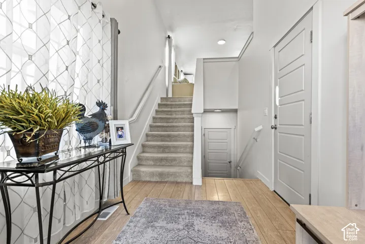 Light wood-finish flooring, carpeted staircase with white handrail, recessed lighting, and white paneled doors
