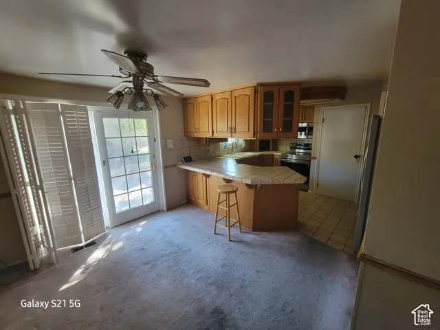 Kitchen with wood cabinetry, tile countertops, and a ceiling fan with integrated lighting