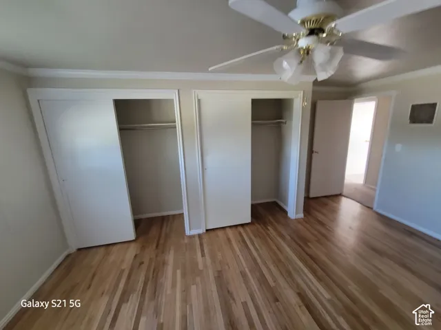 Wood-finish flooring, crown molding, double bi-fold closet doors, ceiling fan with light fixture, and white trim