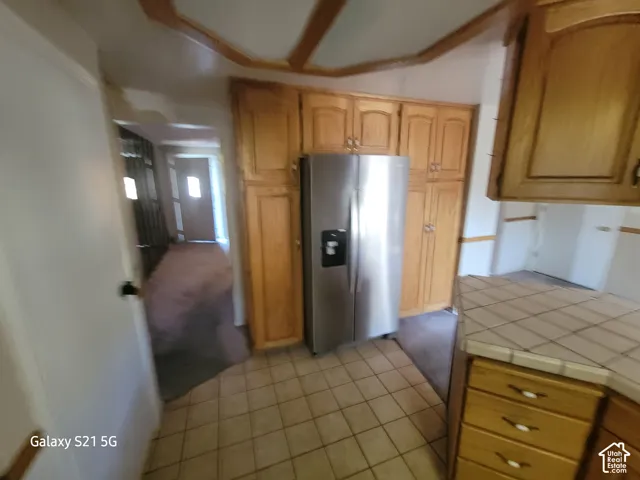 Kitchen featuring wood cabinetry, stainless steel refrigerator, tile countertops, and tile flooring