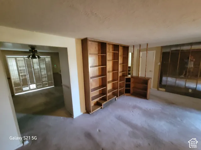 Built-in shelving unit with multiple compartments, wall-to-wall carpeting, and a ceiling fan in the adjacent space