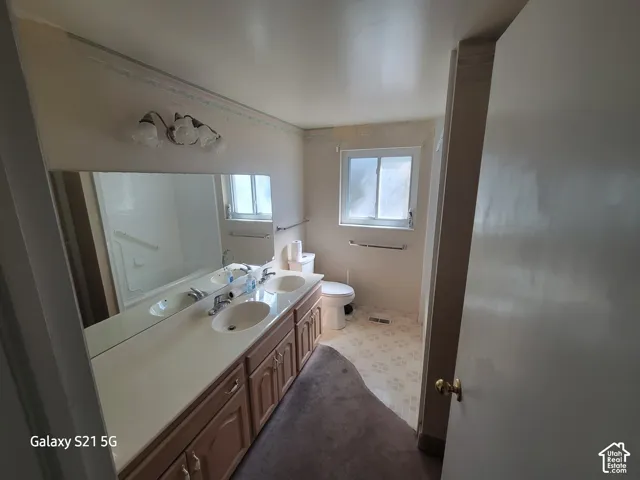 Dual vanity with integrated sinks, wood-finish cabinetry, and an oversized wall mirror