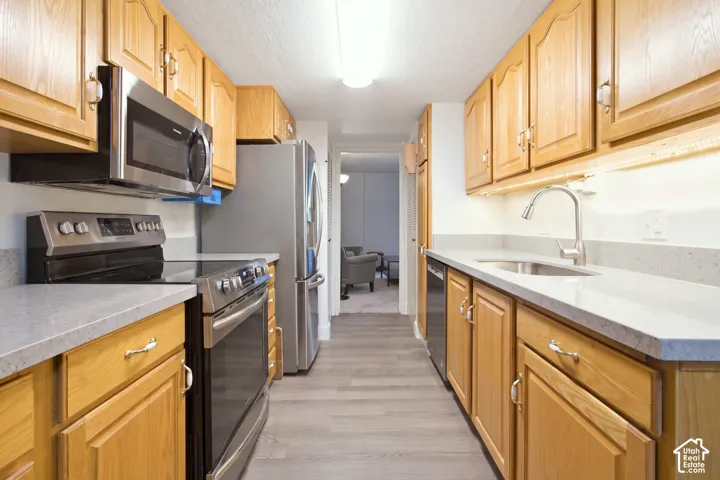 Galley kitchen featuring wood cabinetry, stainless steel appliances, light-toned countertops, and wood-finish flooring
