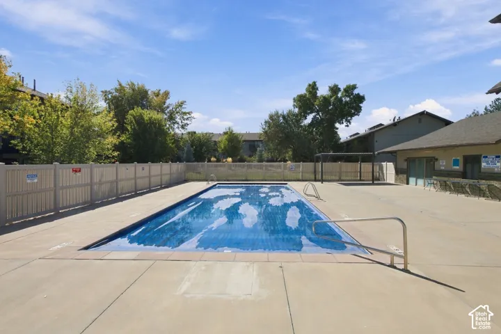 Rectangular swimming pool with a blue cover, surrounded by a concrete deck and a light-colored fence