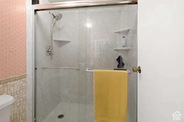 Glass-enclosed shower with a rainfall showerhead, integrated shelving, and a grab bar