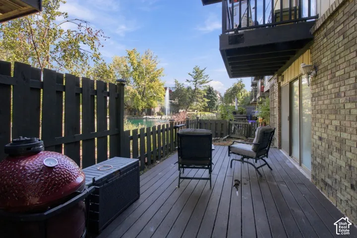 Private ground-level deck with dark wood-finish flooring, brick exterior, and direct access to a water feature with a fountain