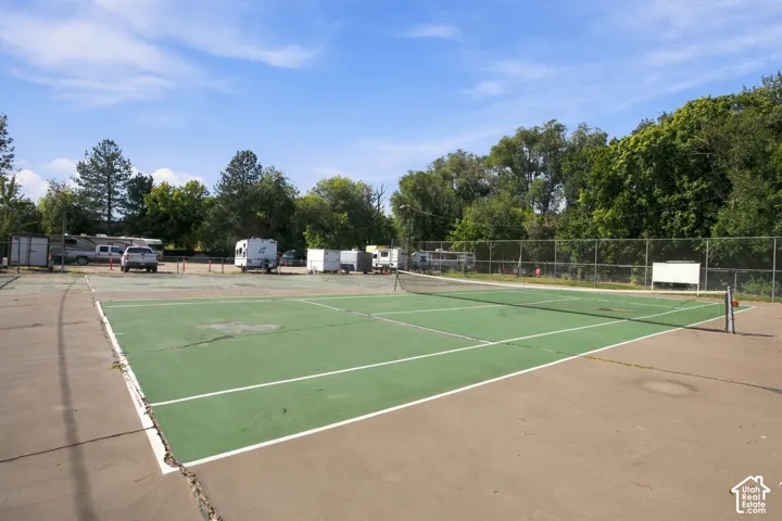 Tennis court with perimeter fencing and surrounding mature trees