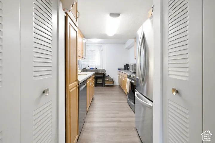 Galley kitchen featuring wood-finish flooring, light wood cabinetry, white countertops, and stainless steel appliances