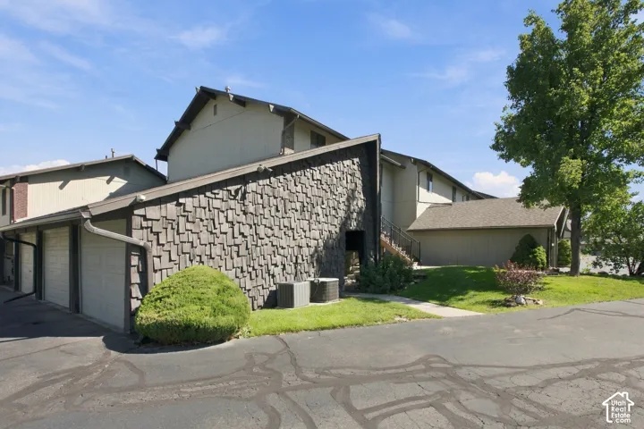 Multi-level building with shingle and horizontal siding, multiple garage doors, and mature landscaping