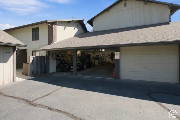 Attached garage with panel door, covered carport, and asphalt shingle roofing