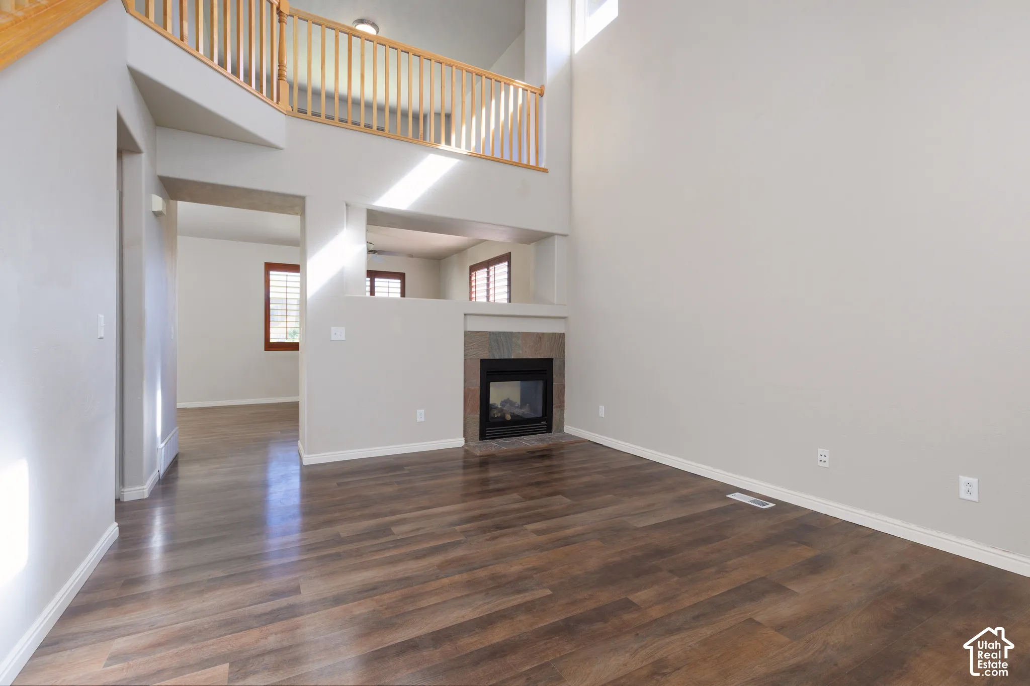 Wood-finish flooring, a two-story ceiling, a built-in fireplace with a tile surround, a second-story open railing, and natural light from upper windows