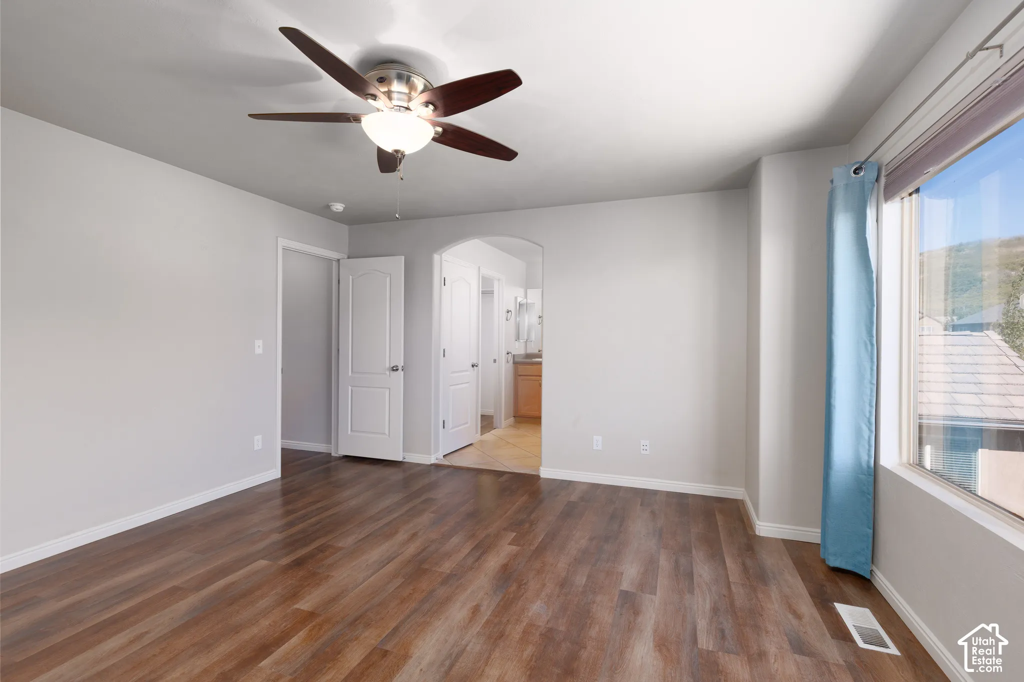 Expansive room featuring wood-finish flooring, a ceiling fan with integrated lighting, and multiple windows